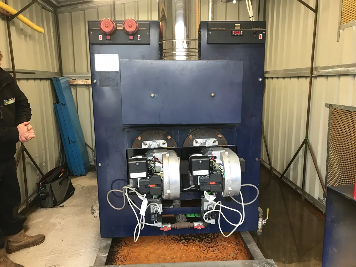 Blue twin-burner boiler with two forced-draught gas burners inside a steel container plant room