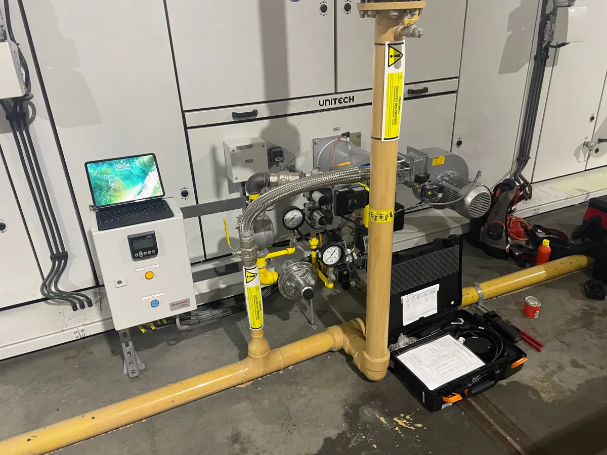 Burner gas train with pressure gauges and control panel on a Unitech unit, with an open test kit case on the floor