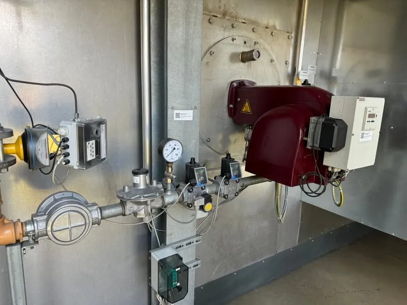 Red forced-draught gas burner with valve train, regulator and pressure gauge on a steel-clad boiler