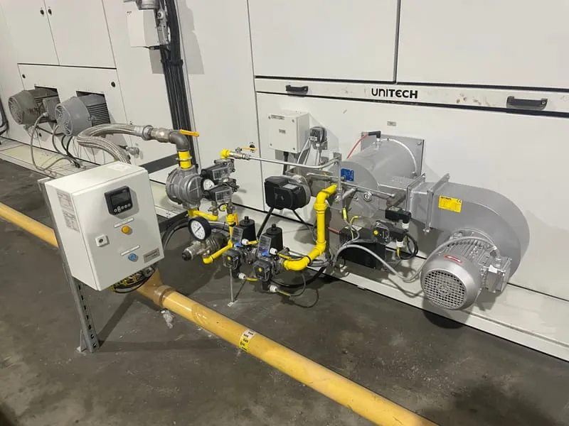 Yellow gas supply pipework and valve train feeding a process burner on a Unitech oven, with control panel