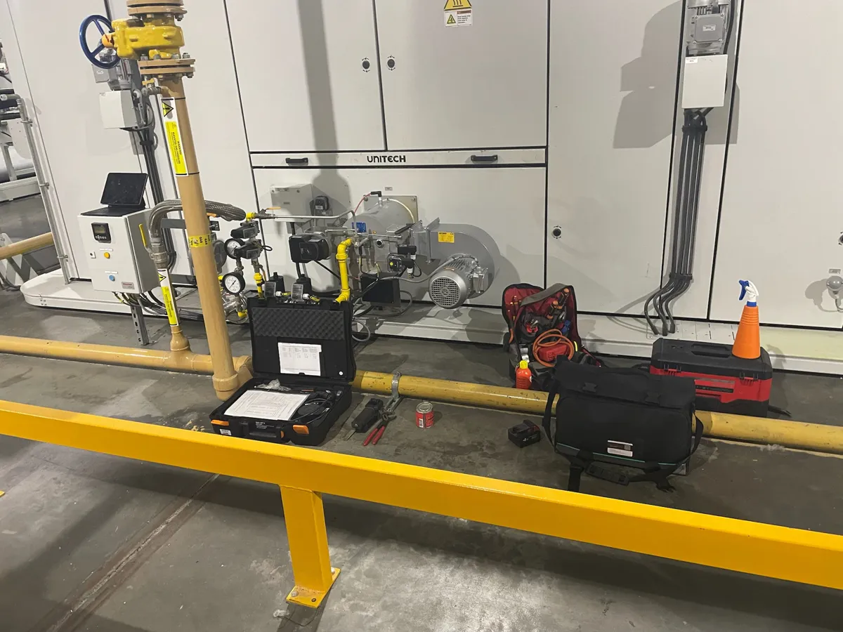 Gas burner fitted to a Unitech unit, with a test kit case and engineer's tools laid out on the factory floor