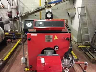 Red commercial boiler with a red forced-draught gas burner in a plant room