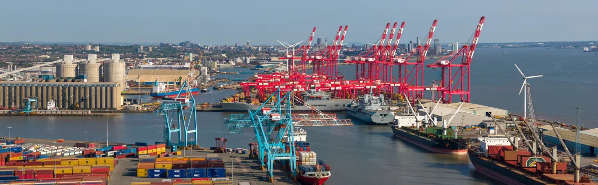 Container port with red quayside cranes, cargo ships and wind turbines on the estuary