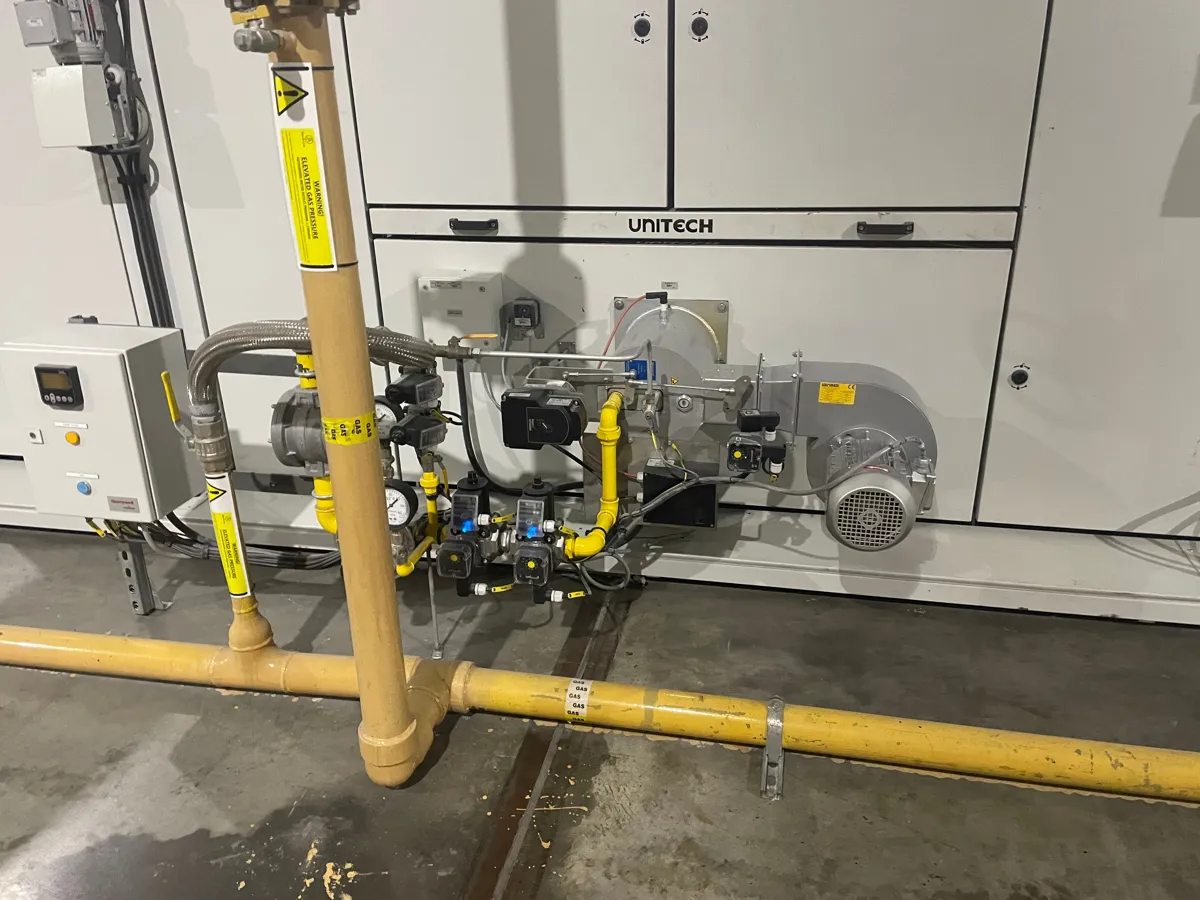 Gas burner and valve train with pressure gauges on a Unitech unit, fed by yellow gas pipework
