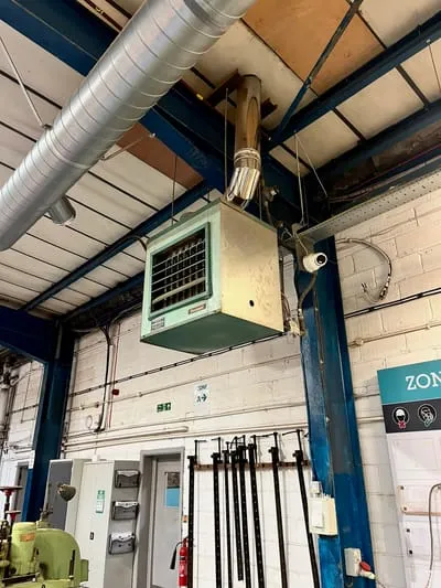 Gas-fired warm air unit heater with flue, mounted high on the wall of a workshop
